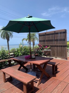 An outdoor patio with a wooden table and benches, a green umbrella, and a view of the ocean. - Suite Terrace Ishigakijima (Ishigaki)