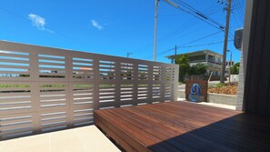 A wooden deck with a metal fence, a hose, and a building in the background. - Yuni no Hama Panari (Miyakojima)
