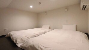 A simple, unadorned hotel room with two single beds, a small window, and a plain white wall. - Yuni no Hama Panari (Miyakojima)