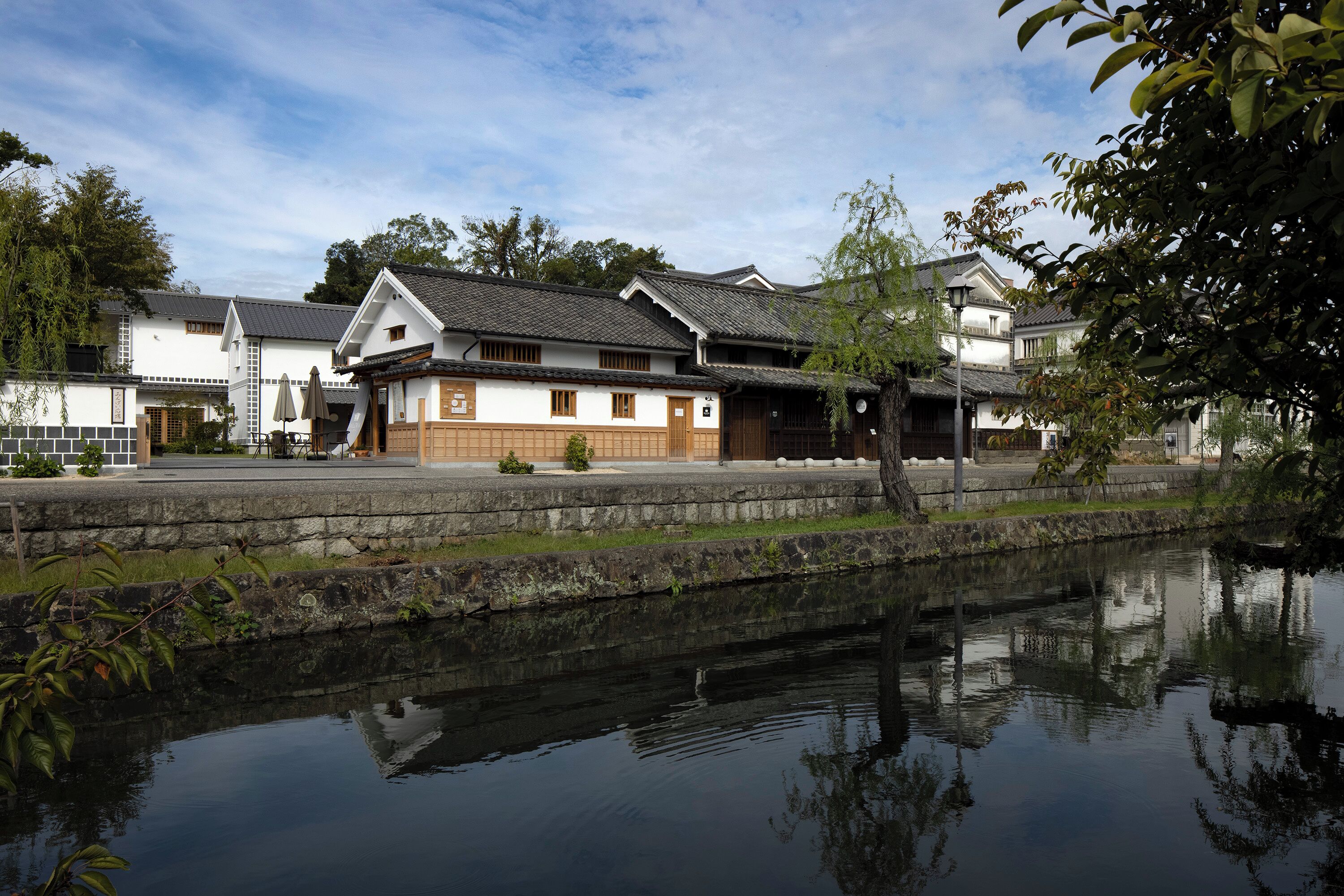 A traditional Japanese-style building with a stone pathway and a calm water body in front.