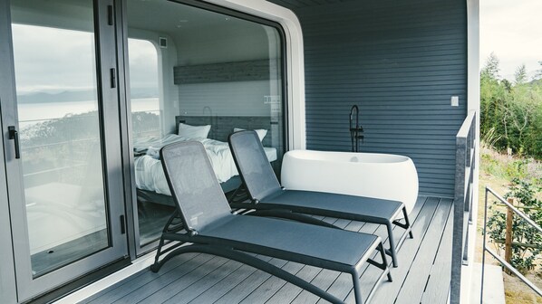 A modern outdoor balcony with a bed, a bathtub, and two lounge chairs. - Hario Beach Walk (Sasebo)
