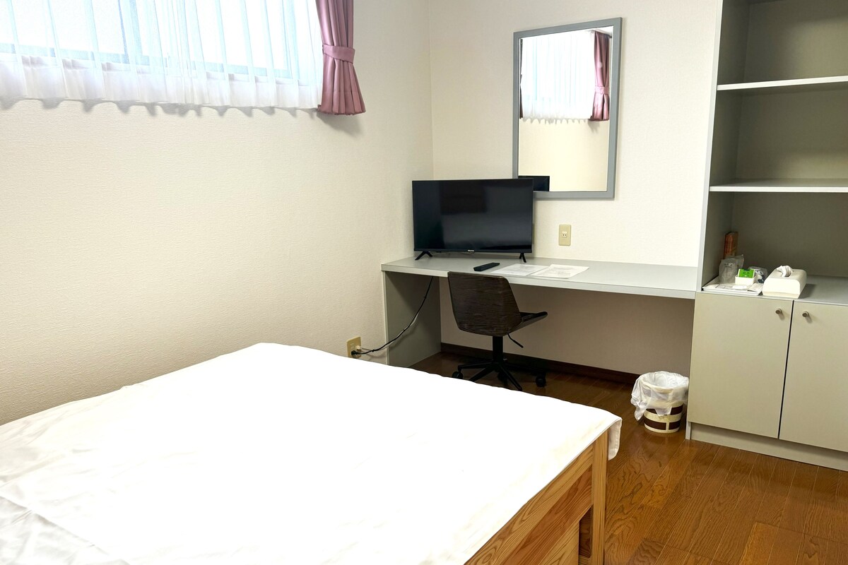 A bedroom with a bed, a desk with a computer, a chair, a mirror, and a wardrobe.