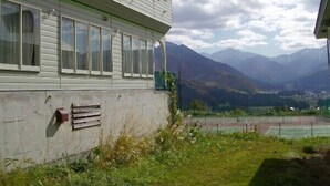 A two-story building with large windows, a concrete foundation, and a view of mountains and a tennis court in the background. - Lodge Soji (Yuzawa)