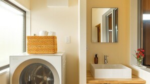 A laundry area with a washing machine and a wicker basket on top, a bathroom with a sink and mirror, and a window with a view. - Temple Hotel Hogenji (Minami-Alps)