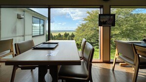 Un coin repas avec une table et des chaises, de grandes fenêtres donnant sur l’extérieur et un tableau encadré au mur.