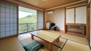 Une pièce de style japonais traditionnel, avec un sol recouvert de tatamis, une petite table basse en bois, des portes coulissantes, une petite télévision et un radiateur.