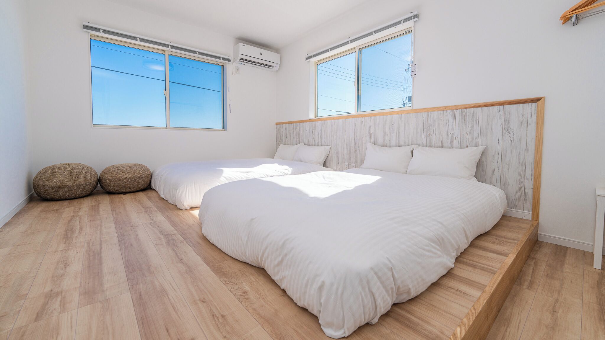 Une chambre avec deux lits, un plancher en bois et de grandes fenêtres.