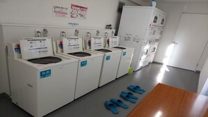 A laundry room with multiple washing machines, a drying machine, and a pair of blue slippers on the floor. - Hotel I-room Rikuzentakata (Rikuzentakata)