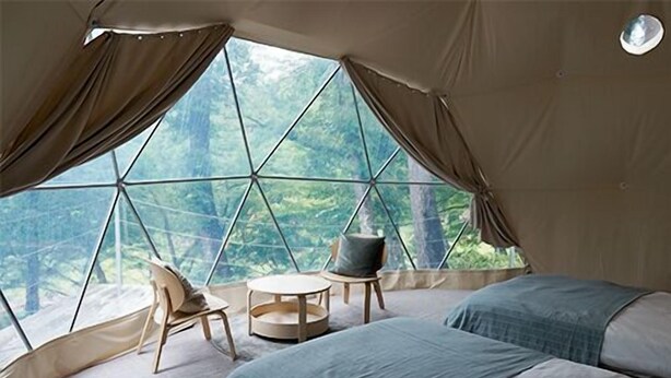 A cozy tent with a large window, two beds, a round table, and a chair. - Hiruzen Shiogama Camping Village (Maniwa)