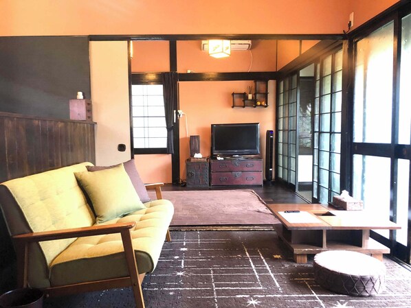 A living room with a sofa, a television, a small table, and a window with blinds. - Rakuan (Hakodate)