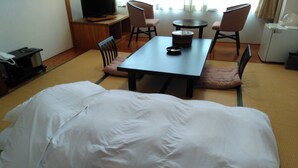 Una habitación con cama, una mesa, sillas, televisor y refrigerador.