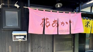 A wooden building with a traditional Japanese entrance, a post box, and a pink banner with Japanese characters.