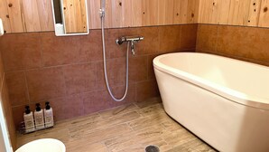 A bathroom with a freestanding bathtub, a showerhead, a toilet, and a mirror.