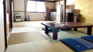 A traditional Japanese room with tatami flooring, a low table, cushions, and a sliding door.