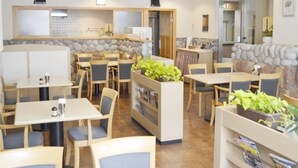 Ein Restaurant mit mehreren Tischen und Stühlen, einer Wand aus Steinplatten und Üanpfanzen in Töpfen.