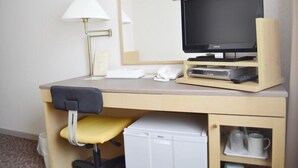 Ein Hotelzimmer mit Schreibtisch, Fernseher, Lampe, kleinem Kühlschrank und Getränkehalter.