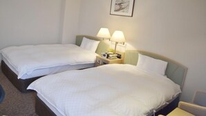 Ein Hotelzimmer mit zwei Einzelbetten, jeweils mit weißer Bettwäsche und Kissen. An den Nachttischen stehen Lampen und eine kleine Uhr. Über den Betten hängt ein gerahmtes Bild.