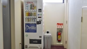 Ein schmaler Korridor mit einem Automaten mit der Aufschrift "KIRIN FIRE" und einem Feuerlöscher an der Wand.