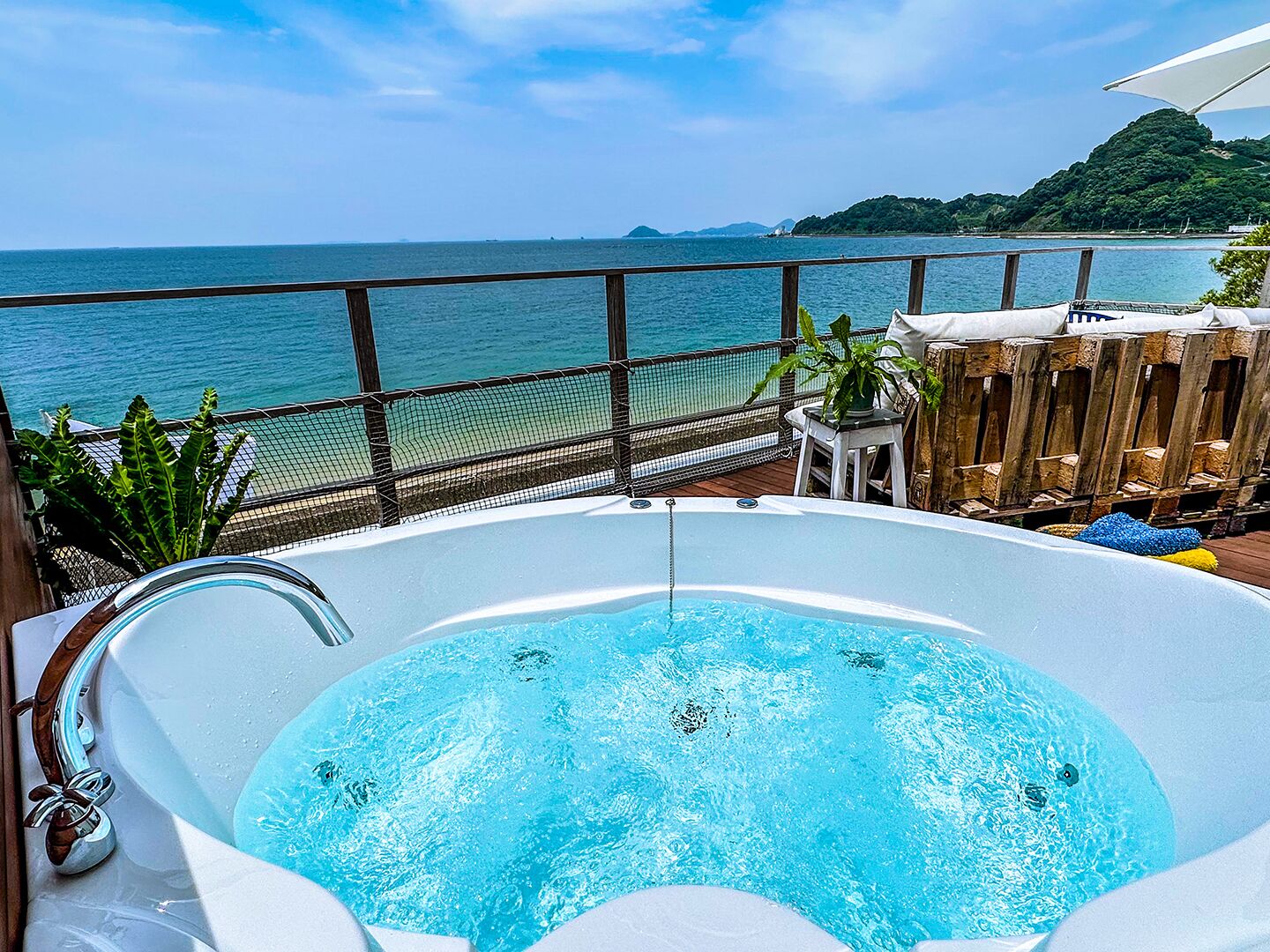 A hot tub with a view of the sea and a wooden deck with plants.