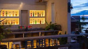 A bar area with illuminated shelves of liquor bottles, a wooden bar counter, and a view of the sea at dusk. - L'art de Vie (Matsuyama)