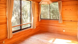 Ein Zimmer mit Holzwänden und Holzböden, zwei mit Vorhängen versehene Fenster und eine schräge Decke.