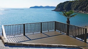 Ein Holzdeck mit Metallgeländer, das auf ruhiges Meer und entfernte Landformen blickt.