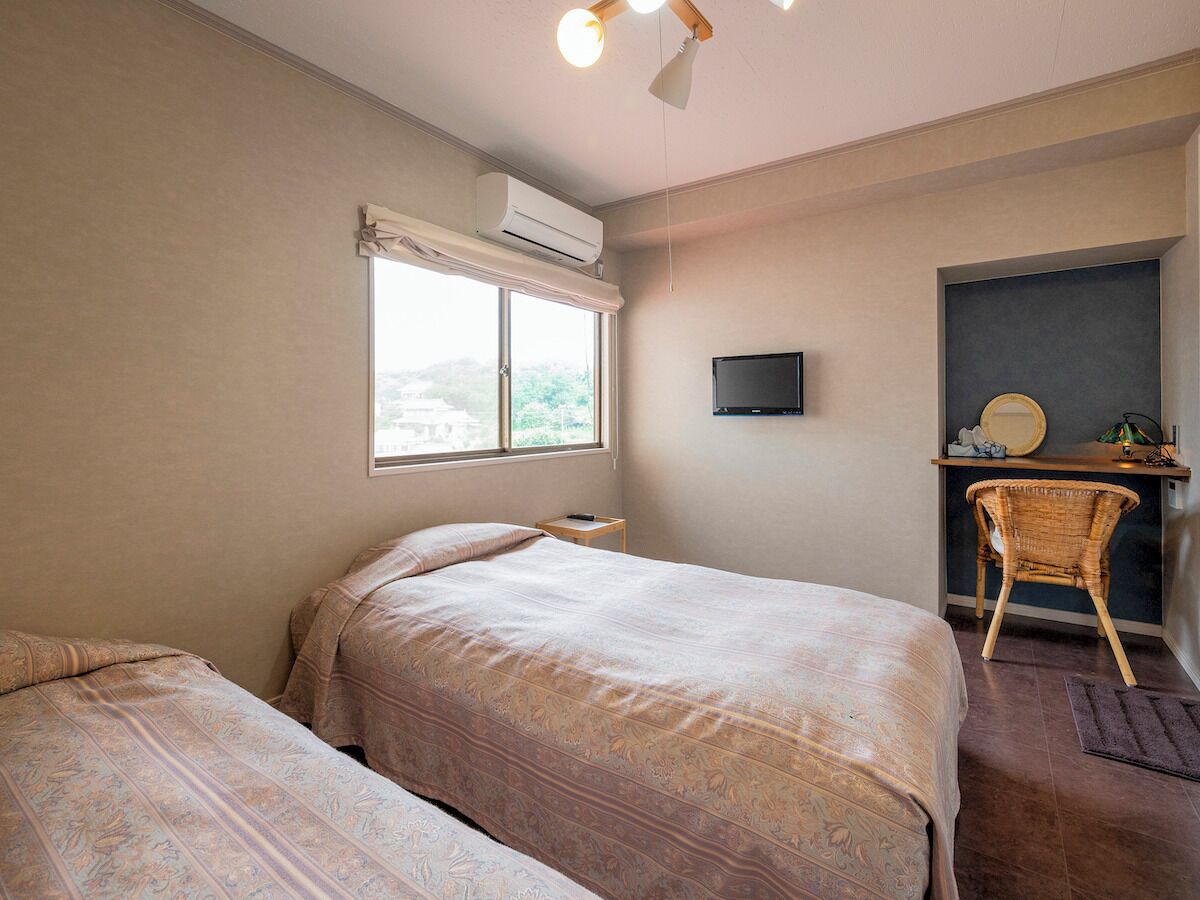 Un dormitorio con dos camas, un escritorio, una silla, un aire acondicionado y un televisor.