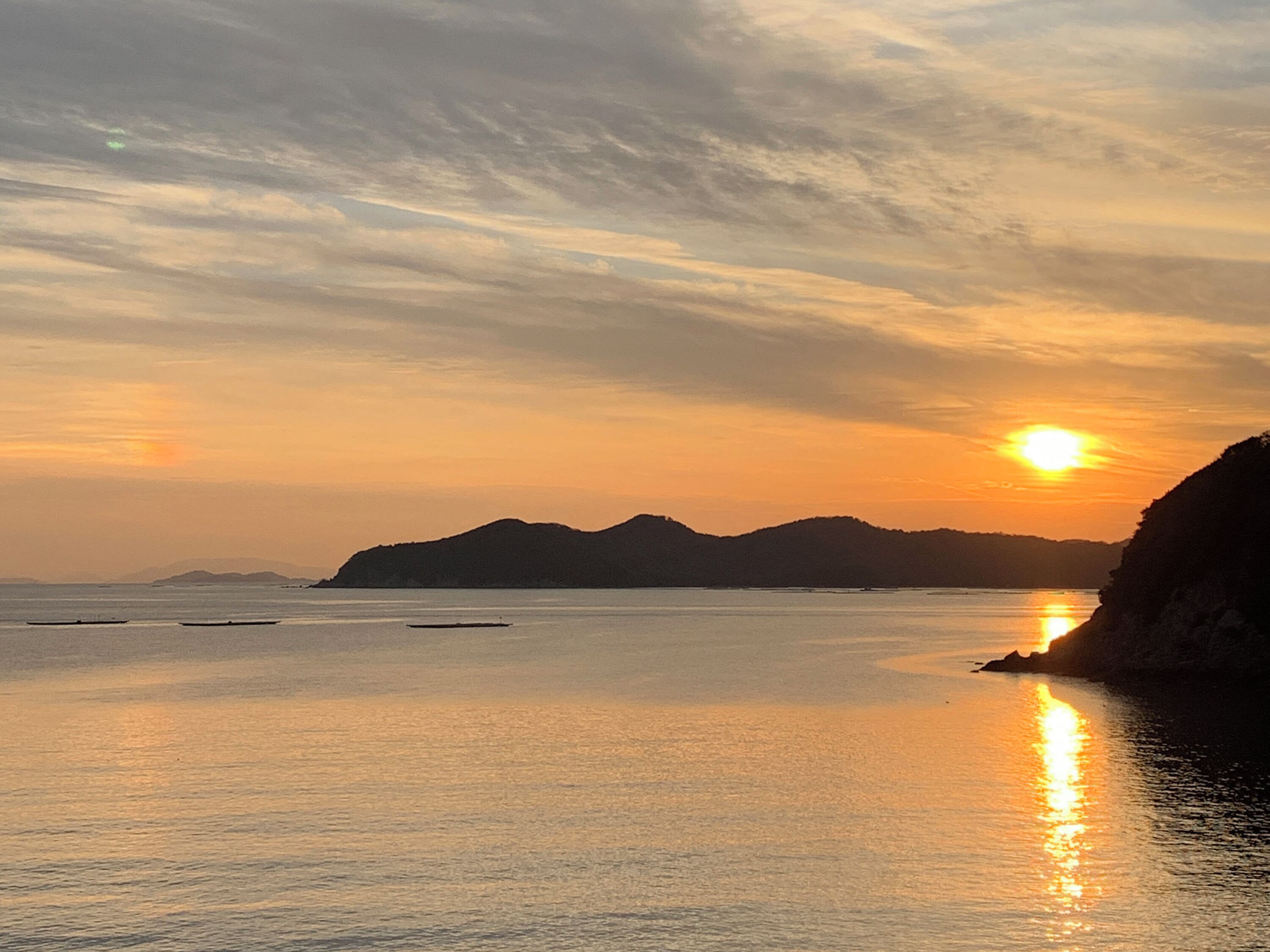 Atardecer costero con aguas tranquilas y montañas a lo lejos.