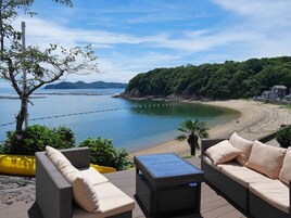 Un patio frente al mar con mobiliario de mimbre y vista a la playa.