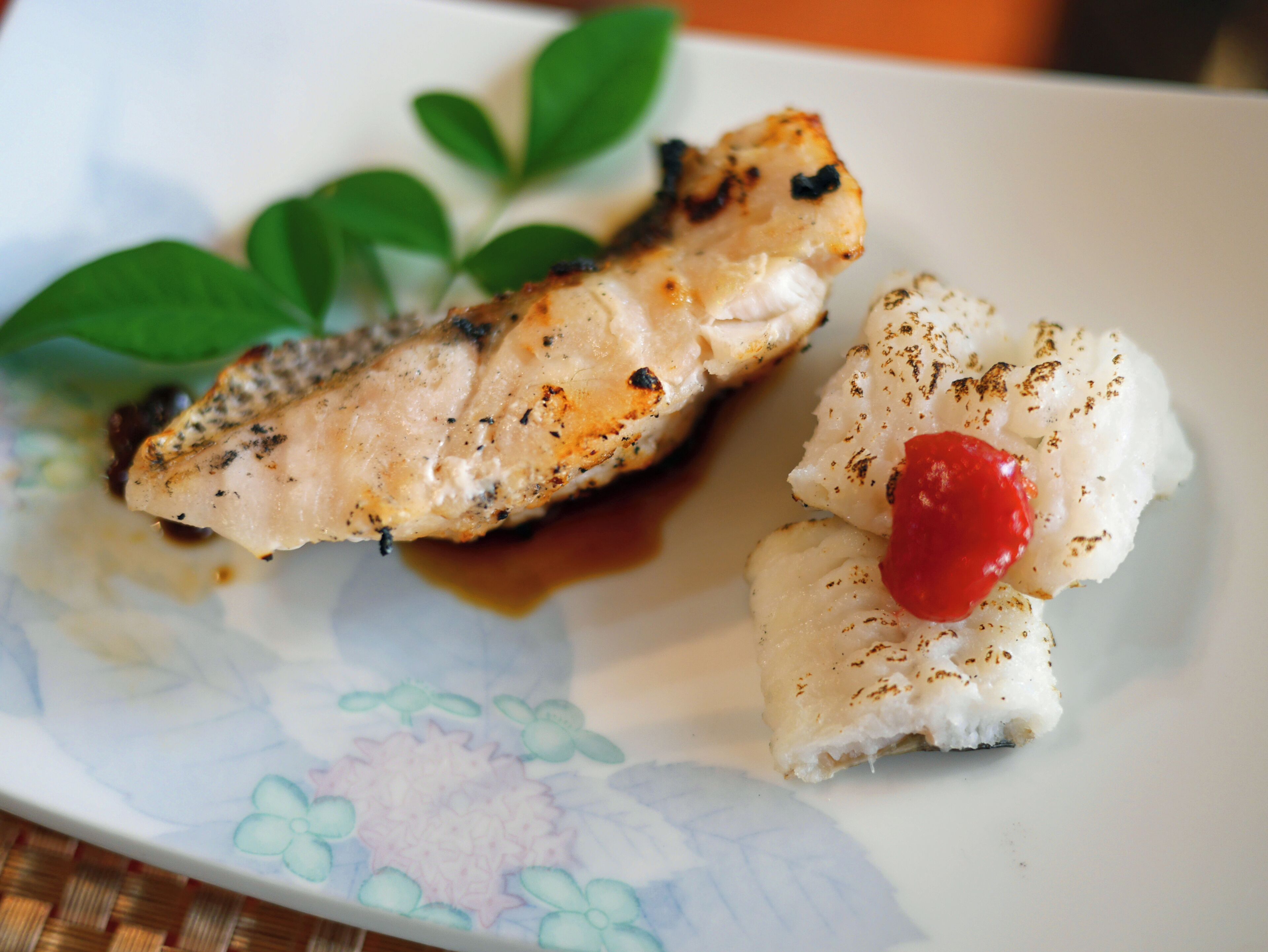 Prato com peixe grelhado e couve-flor, decorado com um pimentão vermelho.