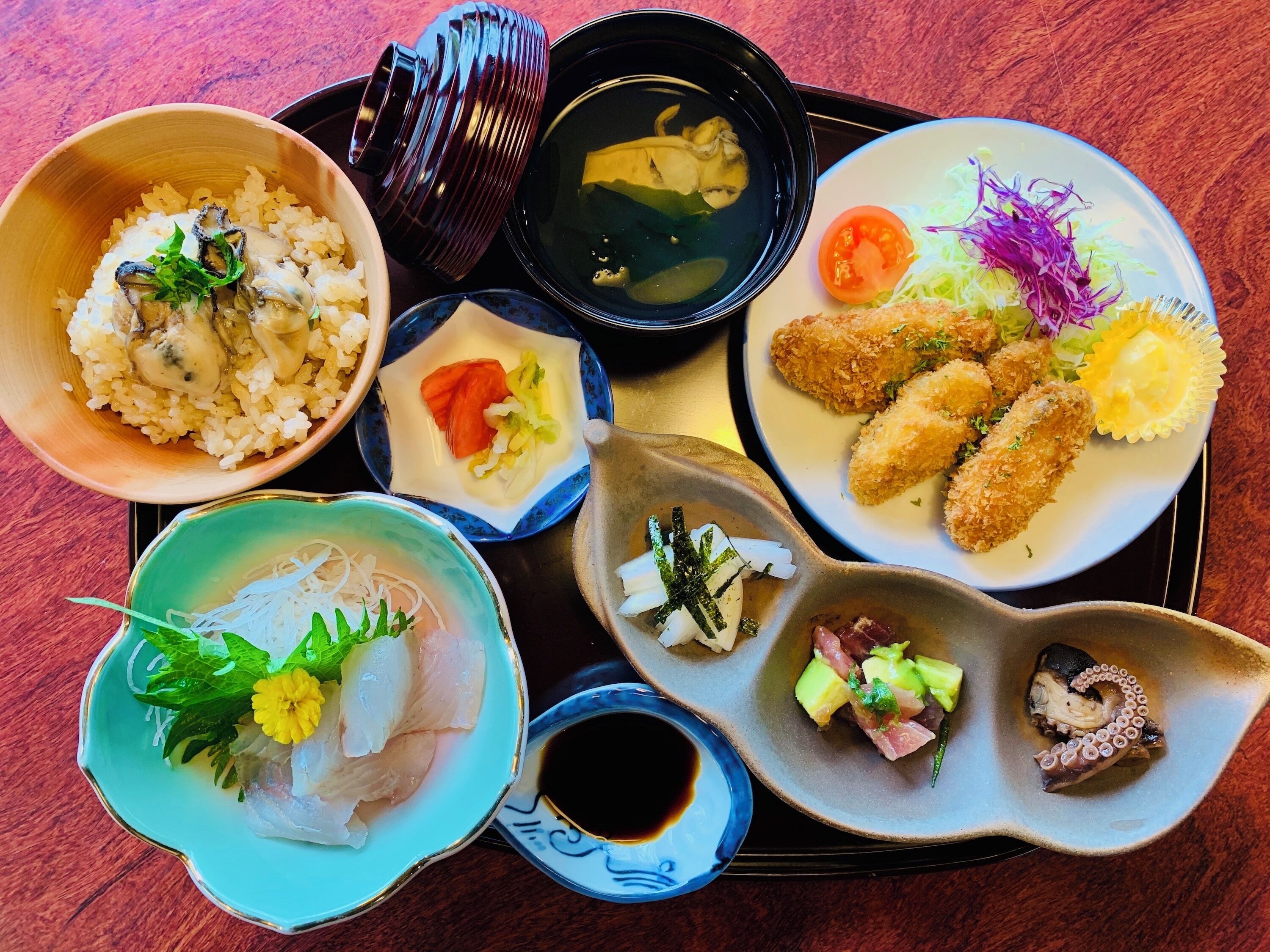 Variedad de platos japoneses, incluyendo arroz, sashimi y tempura, sobre una bandeja.