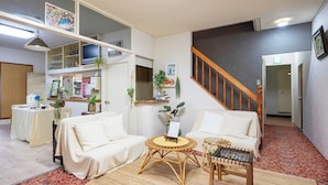 Ein Wohnzimmer mit einer Couch, zwei runden Tischen, einer Treppe und einer Küchenzeile mit Kühlschrank und Spüle.