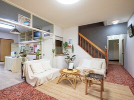 Una sala de estar con un sofá, dos mesas redondas, una escalera y una zona de cocina con un refrigerador y un lavabo.