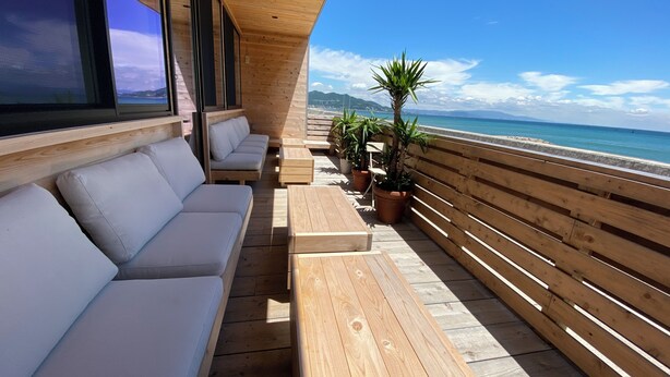 A wooden deck with a sofa and potted plants, overlooking a beach. - Lorchidee Awajishima (Awaji)