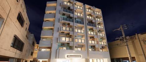 Un hotel de varios pisos con balcones, un cartel que indica que es un hotel y coches aparcados en la entrada.