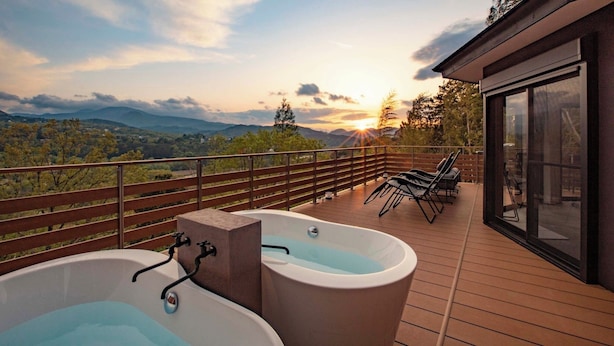 Eine Terrasse mit zwei Whirlpools, einem Holengeländer und Blick auf die Berge bei Sonnenuntergang.