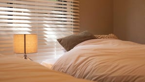 Ein Schlafzimmer mit einem Bett, einer Lampe und Jalousien.