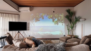 Ein Wohnzimmer mit einem großen Flachbildfernseher, einer Holzbalkendecke und einer gemütlichen Sitzecke mit einer Couch und Kissen.
