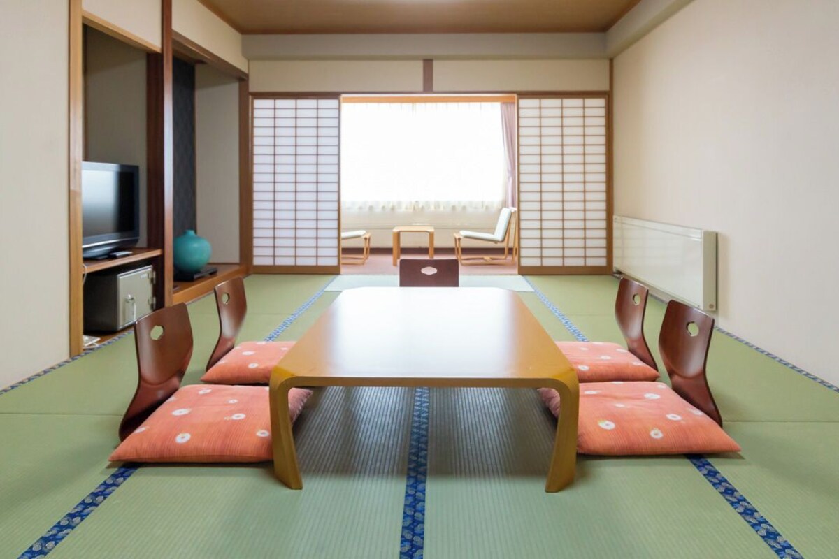 Une pièce de style japonais traditionnel, avec un sol recouvert de tatamis, une table basse et un téléviseur posé sur une étagère.