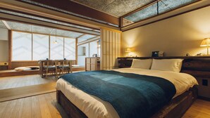 A traditional Japanese-style bedroom with tatami flooring, a low wooden bed, a desk with chairs, and a shoji screen window. - Showcase Hotel Kasane (Gotsu)