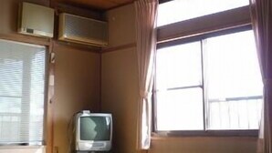 Una habitación con suelo de esteras de tatami, televisión, aire acondicionado y un ventanal con cortinas.