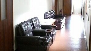 Un pasillo con una fila de sofás de cuero negro y un piano, que conduce a una puerta al final.