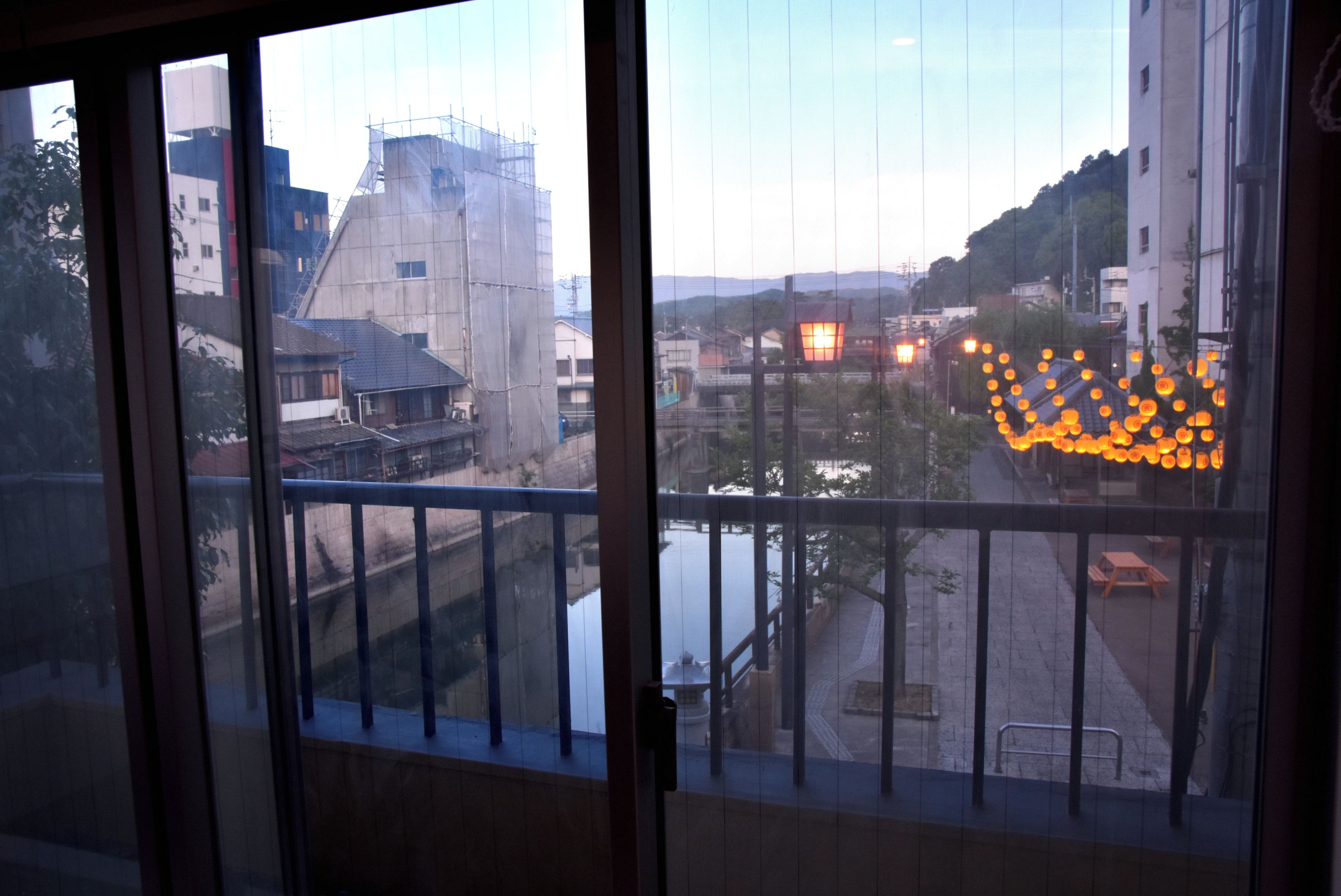 Vista desde una ventana con río, edificios y calle con decoración de faroles tradicionales.