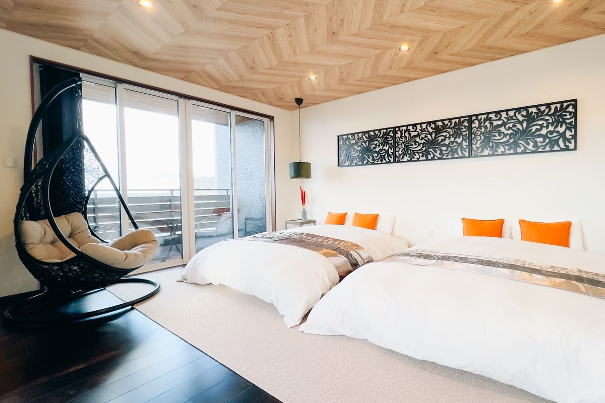 A modern bedroom with a large bed, a hanging chair, and a view of the outdoors.