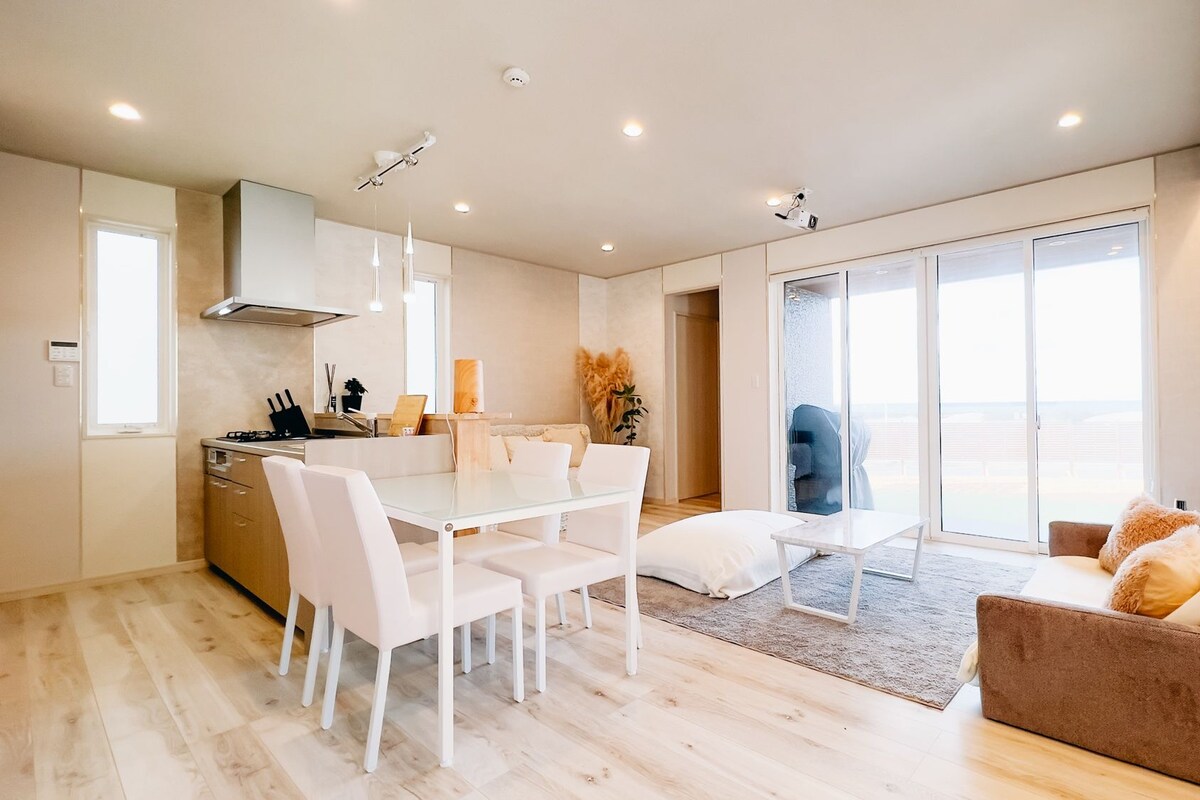 Cocina moderna con armarios blancos, una mesa de comedor con sillas y un amplio ventanal corredizo que da a un balcón.