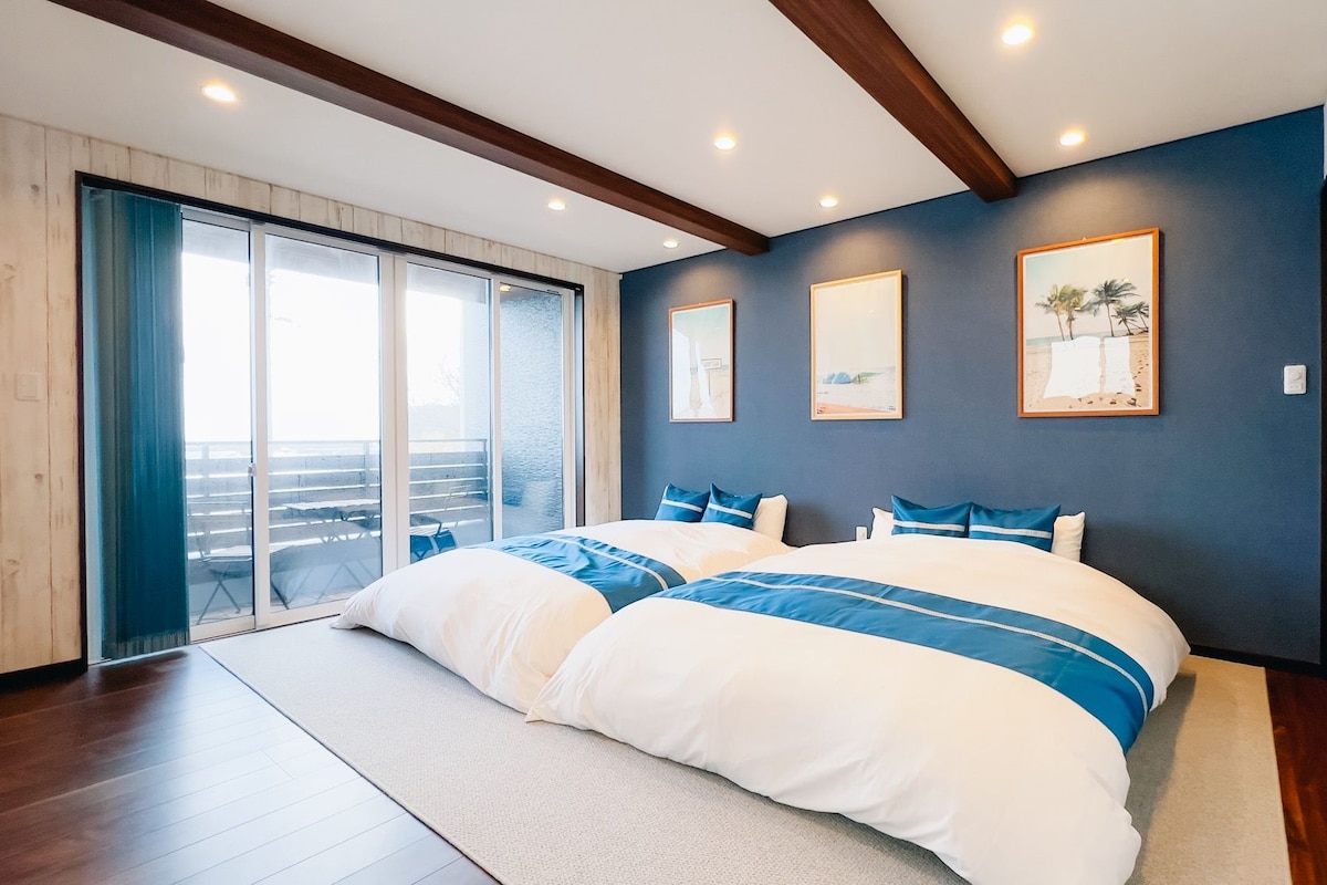 A bedroom with a large bed, a sliding glass door leading to a balcony, and three framed pictures on the wall.