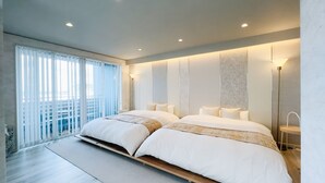 Quarto moderno com duas camas, uma janela grande com persianas e vista para a varanda externa.