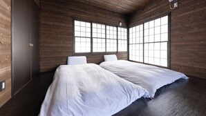 Een kamer met houten wanden, twee bedden met witte lakens en grote ramen met een rasterwerk.
