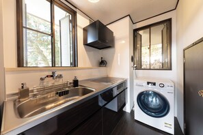 A modern kitchen with a stainless steel sink, a built-in washing machine, and a window with blinds.
