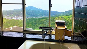 Une salle de bain avec un lavabo et une fenêtre, donnant sur un paysage verdoyant parsemé de bâtiments.